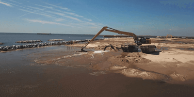 A large marsh buggy on a beach doing dredge work for US Aqua.