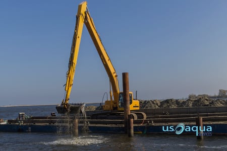 a yellow back hoe dredger on a barge pulling sediment from a large body of water, provided by US Aqua (2)