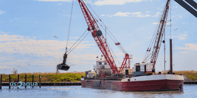 A large boat with dredging equipment in a large channel of water clearing sediment, powered by U.S. Aqua