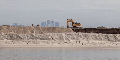 A large excavator on a beach helping in beach reclamation opportunities.