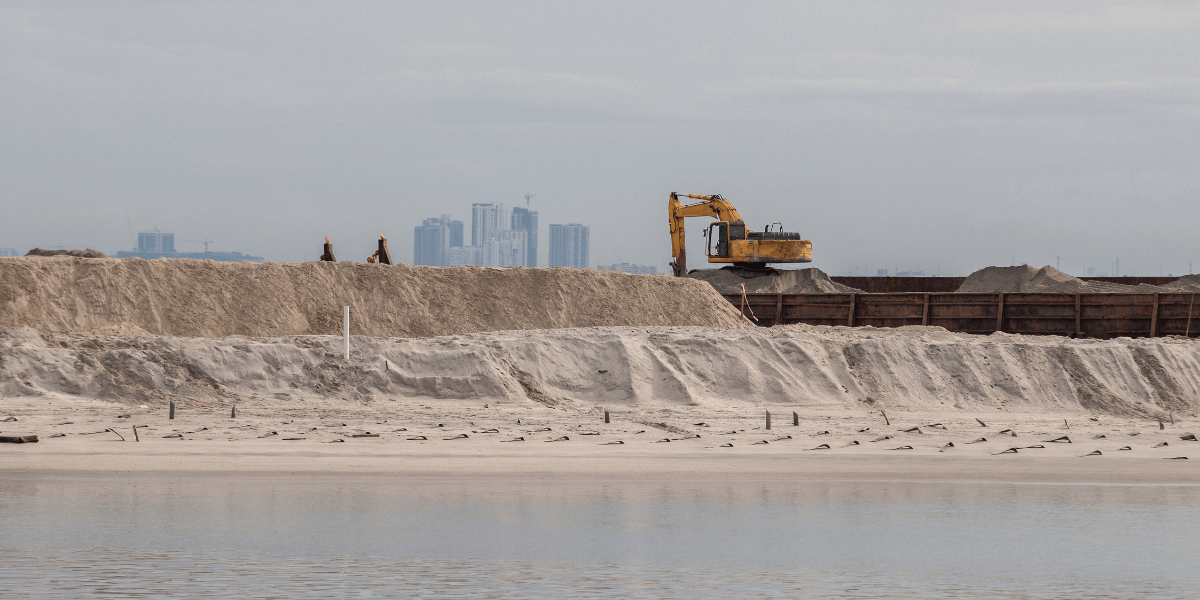 A large excavator on a beach helping in beach reclamation opportunities.