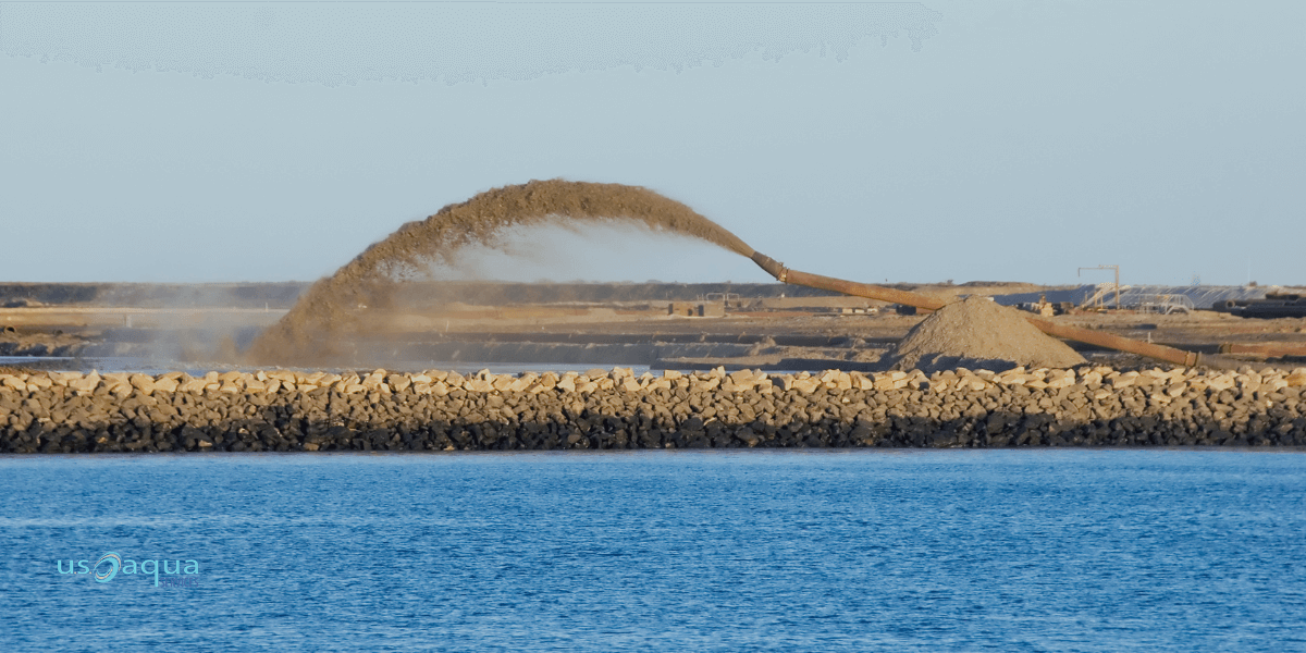 A large pipe shooting sand into a large body of water, dredging services provided by U.S. Aqua services.