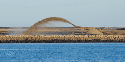 A large pipe shooting sand into a large body of water, dredging services provided by U.S. Aqua services.