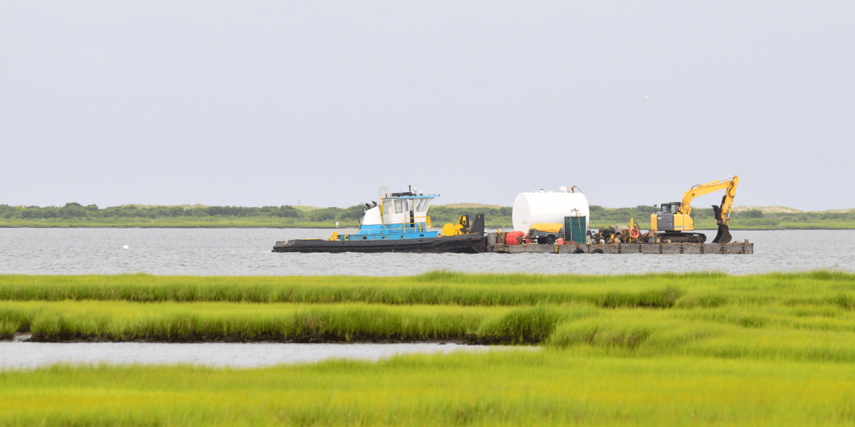 A tug boat with a barge in the marsh that has heavy dredging equipment on it.