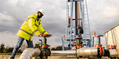 An oilfield worker in a hard hat and yellow jacket closing a valve at an on land oil derrick