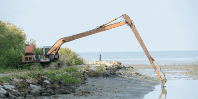 A large excavator in the marsh dredging a waterway.