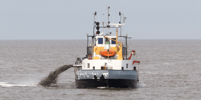 A large dredging ship using jetting equipment to blast sediment in a large body of water.
